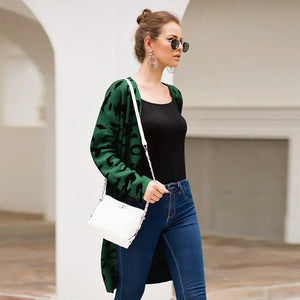 Woman in green animal print cardigan, black top, blue jeans, white purse and sunglasses