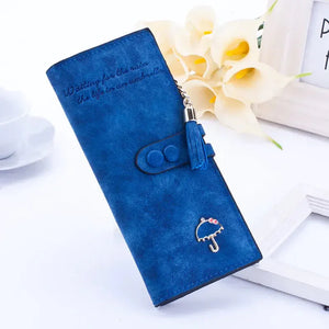 Blue suede women's wallet with tassel and umbrella charm, floral decor background