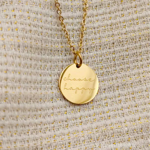 Gold round pendant necklace with engraved choose happy text on textured fabric