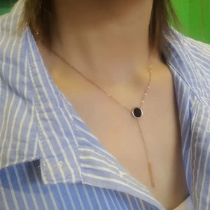 Gold lariat necklace with black circular pendant on model in striped shirt