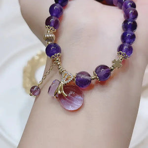 Amethyst bead bracelet with gold accents and a purple gemstone bottle charm on wrist