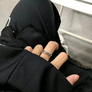 Hand wearing a twisted silver ring, shown on black jeans with frayed edges