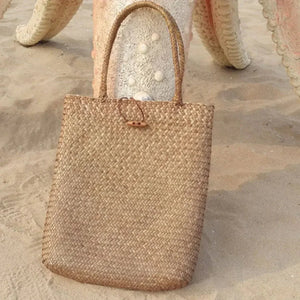 Woven straw tote bag with handles on sandy beach background