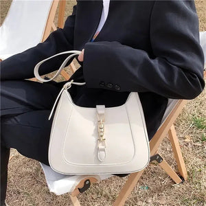 Elegant cream leather shoulder bag with gold buckle detail, styled outdoors on a chair