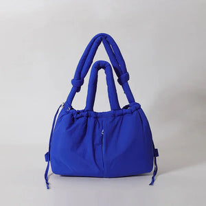 Blue padded fashion handbag with double handles and drawstring detail on light background