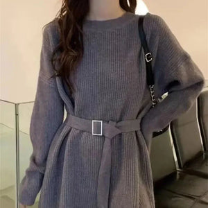Woman in long-sleeve belted gray knit sweater dress, with black shoulder bag