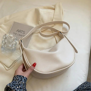 Beige crescent shoulder bag on cream fabric with arts book and glass decor, minimalist style