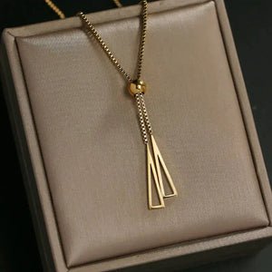 Gold geometric pendant necklace with dual drop triangle charms on a jewelry box