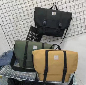 Three canvas messenger bags in black, olive green, and mustard yellow on display