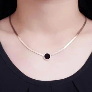 Gold choker necklace with black round pendant worn on woman’s neck