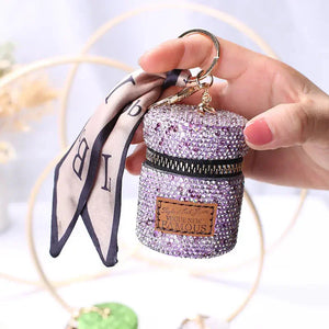 Hand holding a small purple rhinestone keychain pouch with scarf and zipper closure