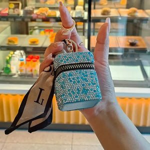 Hand holding a small blue rhinestone-studded pouch keychain with a silk scarf accent