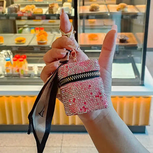 Hand holding a pink rhinestone mini bag keychain with zipper in a bakery setting