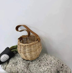 Woven rattan handbag with brown leather handle on stone, minimalist style