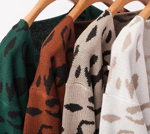 Leopard print knit sweaters in green, brown, beige, and white on wooden hangers