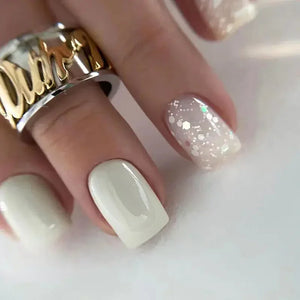 Hand with white and glittery manicure, wearing a chunky gold and silver ring