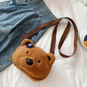 Plush bear-shaped kids shoulder bag with brown strap, denim skirt and sneaker on bed