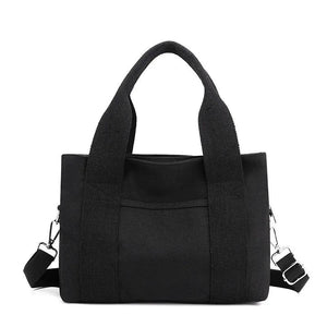Black canvas tote bag with dual handles and adjustable shoulder strap on white background