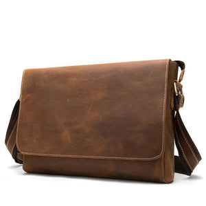 Brown leather messenger bag with adjustable strap and brass hardware on white background