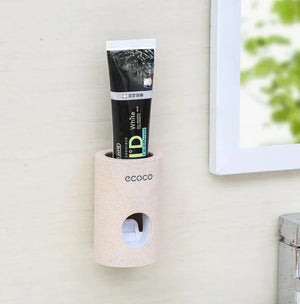 Wall-mounted beige toothpaste dispenser holder with tube in a modern bathroom.