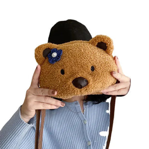 Woman holding fuzzy bear-shaped purse with blue flower accessory, wearing blue sweater