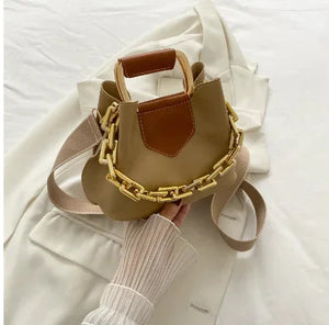 Beige and brown mini handbag with chunky gold chain, held over a cream blazer.
