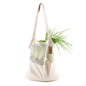 Reusable cotton mesh tote bag filled with fresh green vegetables on white background