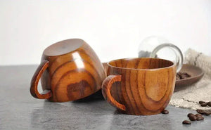 Pair of wooden coffee cups with handles on marble surface, coffee beans nearby