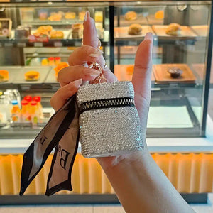 Hand holding a sparkly rhinestone mini bag keychain with a zipper and attached ribbon