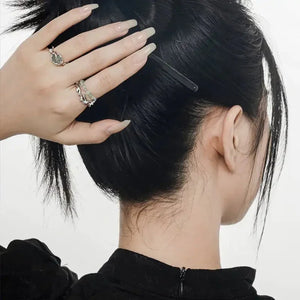 Woman with manicured nails and gemstone rings holding up her black hair with a hairpin