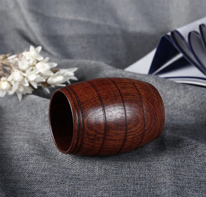 Polished wooden cup shaped like a barrel on gray fabric, with flowers and a book nearby