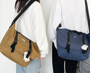 Two people wearing white tops with large crossbody messenger bags, one tan and one navy blue.