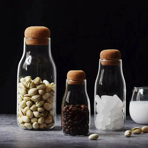 Glass storage jars with cork lids filled with pistachios, coffee beans, and sugar cubes