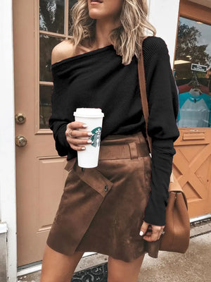 Woman in black off-shoulder sweater and brown suede mini skirt holding coffee outdoors