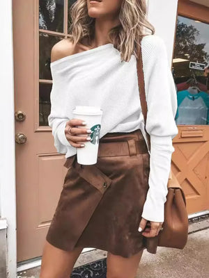 Woman in white off-shoulder sweater and brown suede skirt holding coffee outside shop