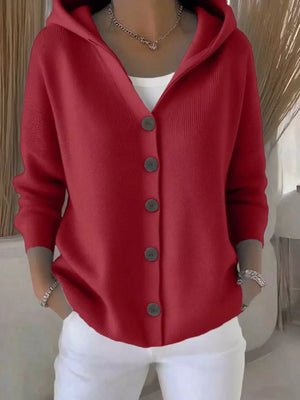 Woman wearing a red hooded cardigan with buttons, white pants, and silver jewelry