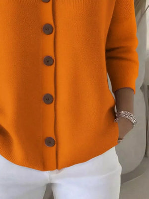 Bright orange button-up sweater with brown buttons, white pants, silver bracelet