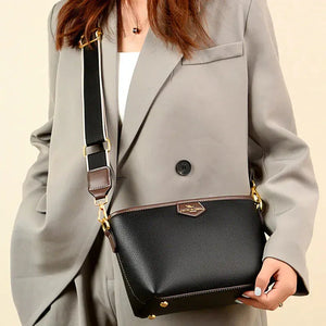 Woman wearing a gray blazer holding a black leather crossbody bag with gold accents