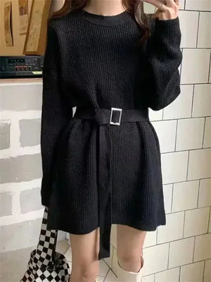 Woman wearing a black knit belted sweater dress, holding a checkered tote bag, fashion outfit