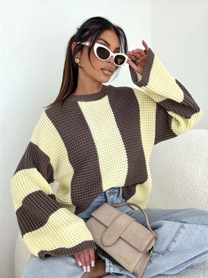 Woman wearing oversized striped knit sweater, cat eye sunglasses, light blue jeans, and holding a beige Jacquemus handbag