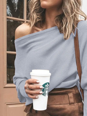Woman wearing light blue off-shoulder sweater and brown pants holding a coffee cup