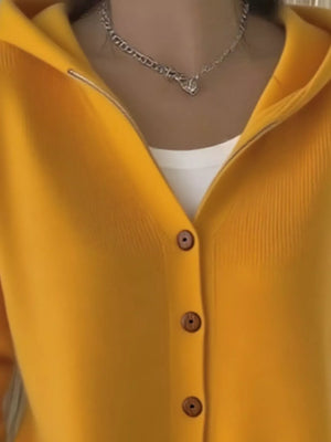 Woman wearing a yellow button-up cardigan, white top, and silver chain necklace