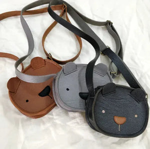 Three bear-shaped kids crossbody bags in brown, light gray, and dark gray on white fabric