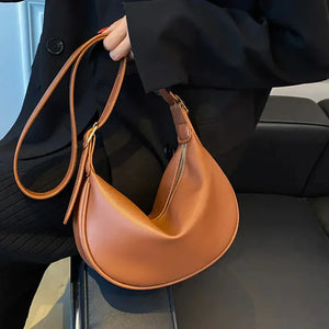 Woman holding a brown leather crescent shoulder bag with zipper, modern fashion accessory