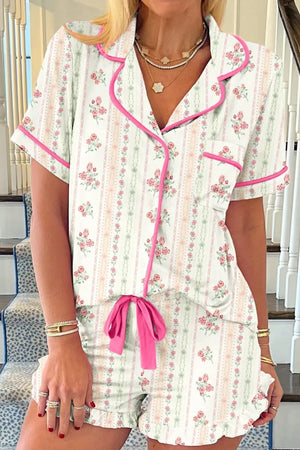 Woman wearing floral print short sleeve pajama set with pink trim and drawstring shorts