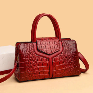 Red crocodile-embossed leather handbag with top handles and shoulder strap on beige background
