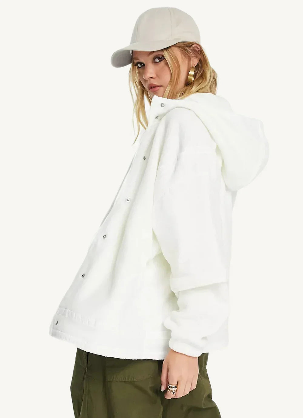Woman in white hooded jacket and beige cap, wearing gold hoop earrings, side pose