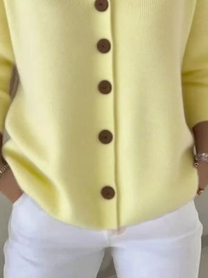 Yellow button-up cardigan with long sleeves, styled with white pants.