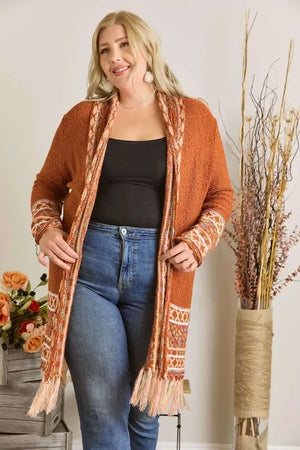 Woman in autumn cardigan with fringe, black top, and jeans, posing indoors with floral decor