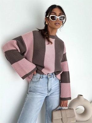 Woman in oversized pink and brown striped knit sweater, light wash jeans, white sunglasses, holding beige handbag